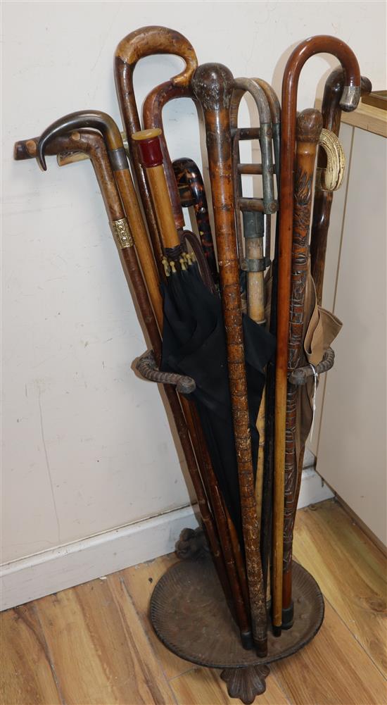 A collection of walking sticks, canes, shooting sticks, parasols and a cast iron stick stand